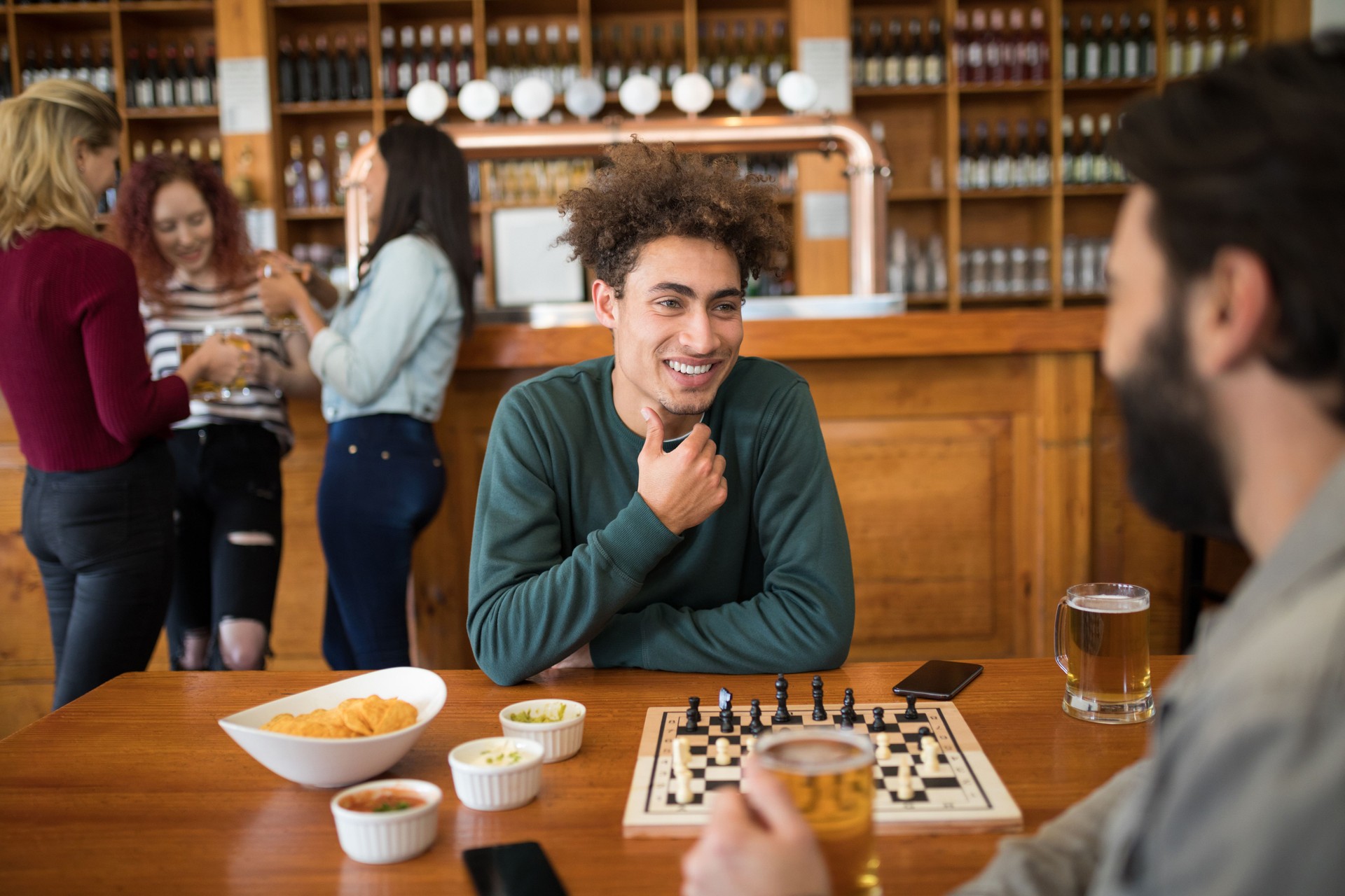 Two adult men playing chess while having glass of beer